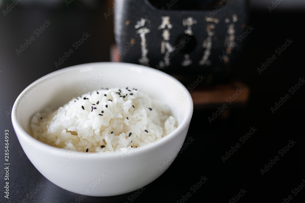 Japanese cooked rice in a white bowl on black table.