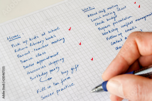 To do list. Concept of work/life balance. Close-up of a man's hand with  pen keeping track of a handwritten list of home and work-related tasks.