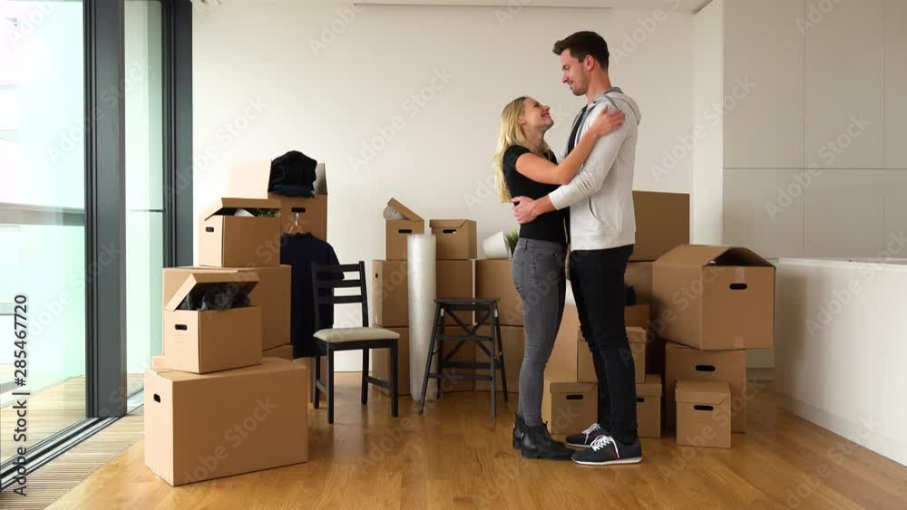 A happy moving couple hugs in a new apartment - piles of cardboard boxes in the background A happy moving couple hugs in a new apartment - piles of cardboard boxes in the background