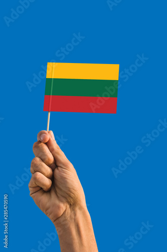 Woman hand holding Lithuania flag with stick, waving flag on deep blue sky. National theme, deep blue sky.