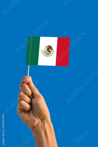 Woman hand holding Mexico flag with stick  waving flag on deep blue sky. National theme  deep blue sky.