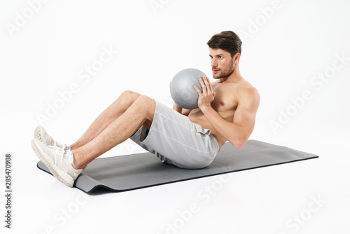 Concentrated strong young sports man isolated over white wall background make exercise with ball. photo