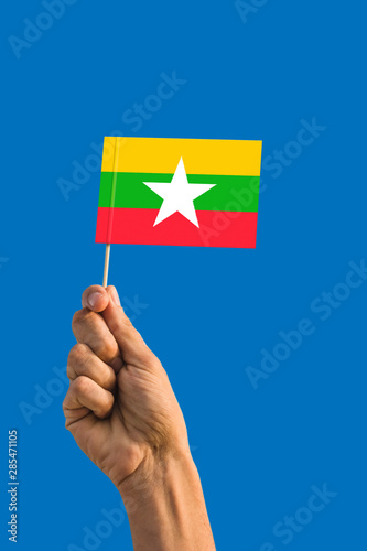 Woman hand holding Myanmar flag with stick  waving flag on deep blue sky. National theme  deep blue sky.