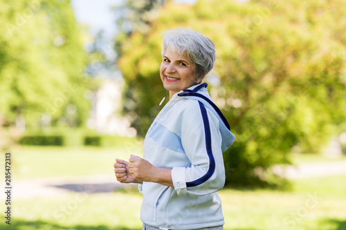 fitness, sport and healthy lifestyle concept - senior woman with earphones running along summer park