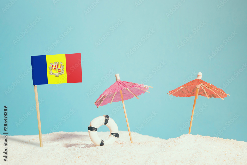 Miniature flag of Andorra on beach with colorful umbrellas and life preserver. Travel concept, summer theme.