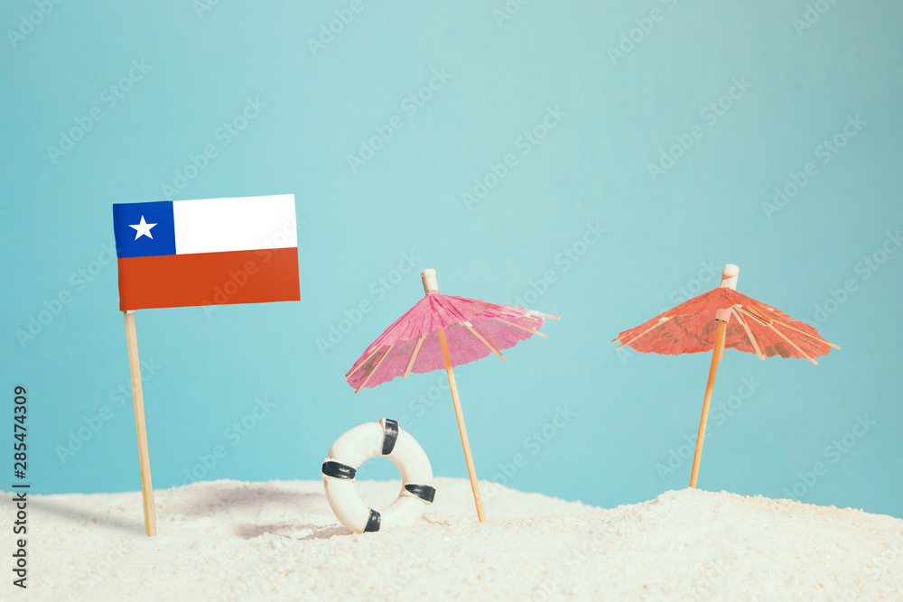 Miniature flag of Chile on beach with colorful umbrellas and life preserver. Travel concept, summer theme.
