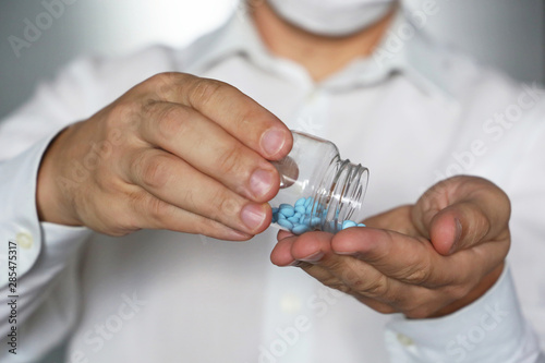 Doctor giving pills, physician in medical mask holding in hands bottle with blue tablets. Concept of dose of drugs, vitamins, viagra, pharmacy, anti-inflammatory photo