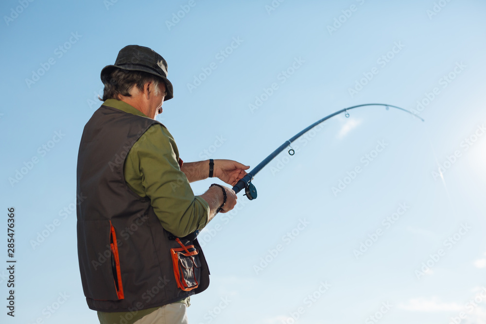 Retired man pulling fishing tackle after catching fish Retired man pulling fishing tackle after catching fish