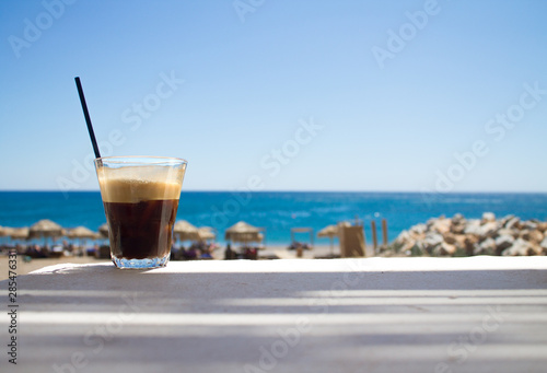 glass with ice coffee fredo espresso or frappe on the corner of the table with beach on background
