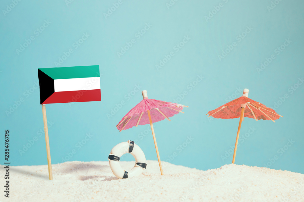 Miniature flag of Kuwait on beach with colorful umbrellas and life preserver. Travel concept, summer theme.