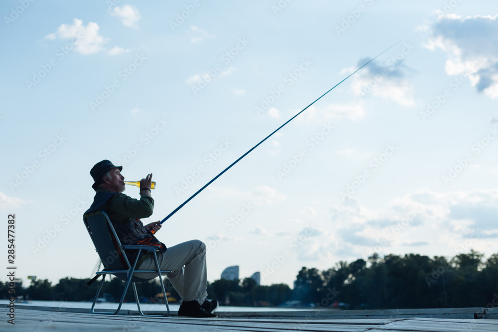 Retired man feeling peaceful while catching fish and drinking beer Retired man feeling peaceful while catching fish and drinking beer