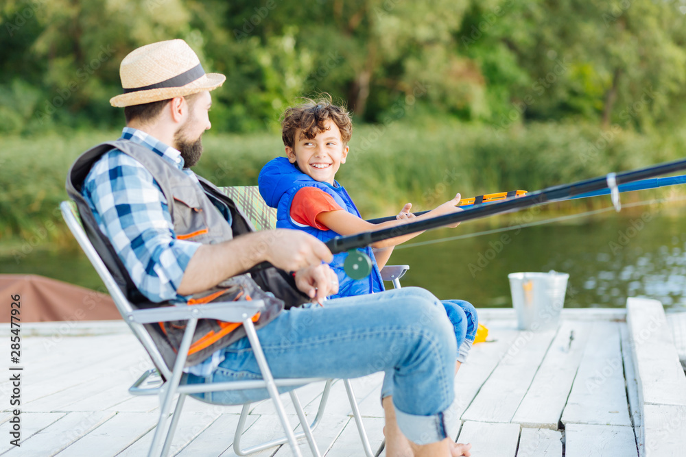 Son looking at father while fishing together near lake Son looking at father while fishing together near lake