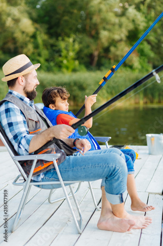 Father and son sitting in chairs while fishing in the morning