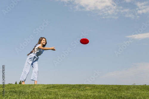 Long shot little girl playing with red frisbee