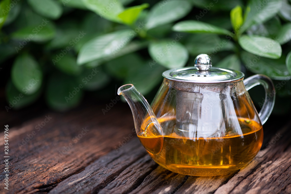 The hot tea with glass teapot on the wooden and green leaf background. Herbal tea with Chrysanthemum.