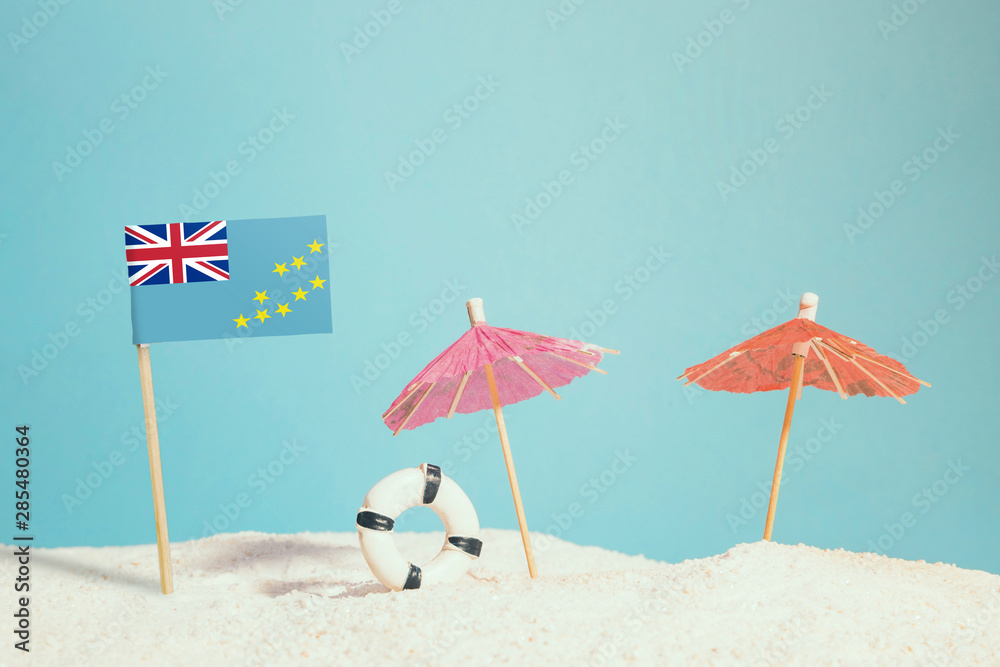 Miniature flag of Tuvalu on beach with colorful umbrellas and life preserver. Travel concept, summer theme.