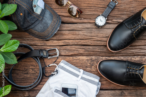Men fashion clothing set and accessories on rustic wooden background include black shoes, belt, phone, hat, sunglasses, shorts and watch. Flat lay, top view