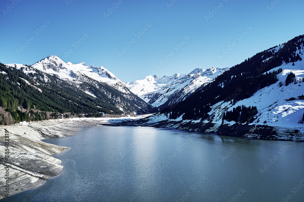 panoramic view of a reservoir lake at winter with cracked mud around. Water in the high alps in austria by day with beautiful light.