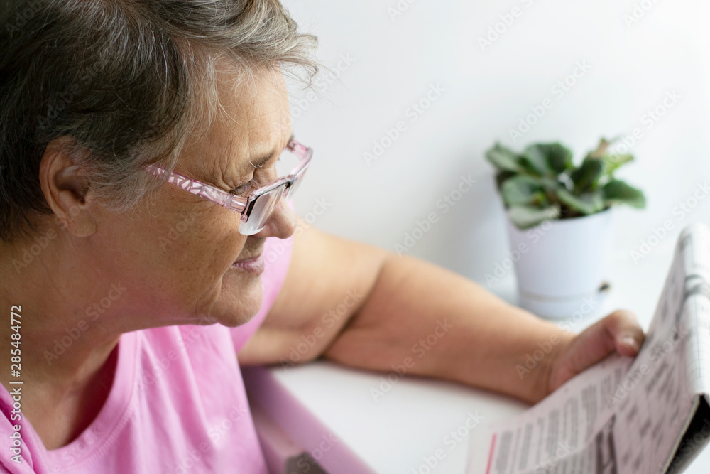 Poor eyesight of an old woman. An old woman reading a newspaper with glasses.