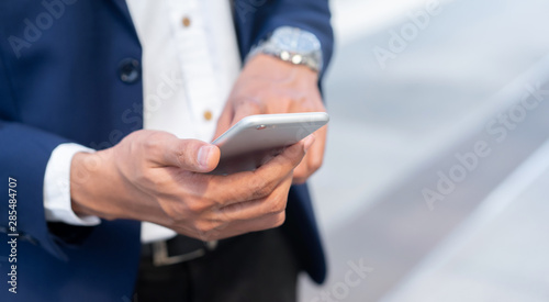 close up businessman hand holding smart phone (mobile device) to checking business news on website such as stock market, currency exchange ,global financial and email alert form company at office