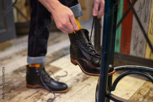 Man tie shoelaces on black leather boots indoor close up view