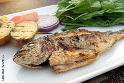 Turkish or Greek restaurant main course, sea bream fish grilled food dinner cuisine culture. Delicious grilled sea bream fish with vegetable, onion and potatoes.