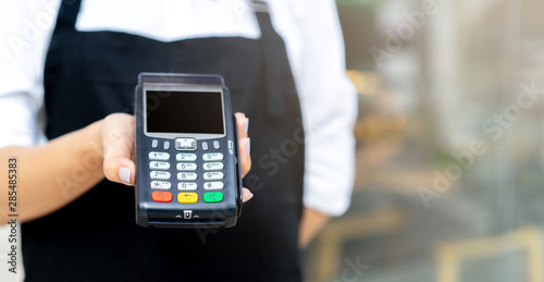 close up waitress worker hand showing an electronic banking money machine for receiving purchase from customer outside the restaurant shop , business and technology of contactless payment concept 