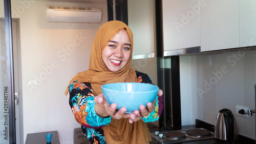 Portrait of beautiful asian muslim woman, housewife carrying bowl to serve at camera