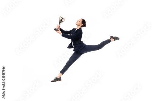 happy businesswoman holding trophy cup while jumping in dance isolated on white