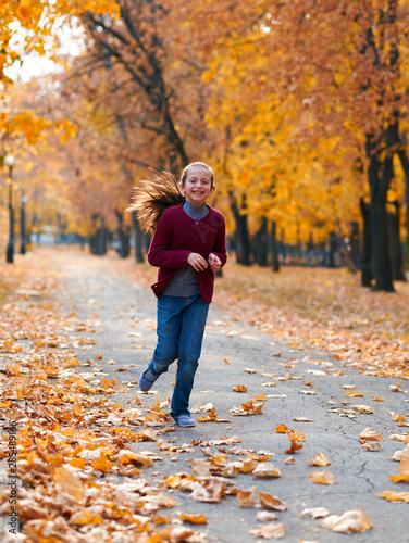 Happy child girl running, playing, posing, smiling and having fun in autumn city park. Bright yellow trees and leaves © soleg