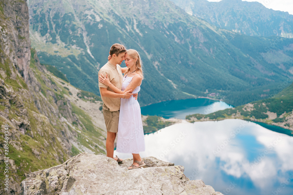 Naklejka premium Happy loving couple standing together at stone in High Tatra national park in Poland with a picturesque landscape on background.