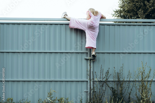 Girl climbing metal fence outdoor. Curious child on high white painted gates. Naughty kid playing outside, breaking rules. Childhood and youth concept. Restless teen entering private property