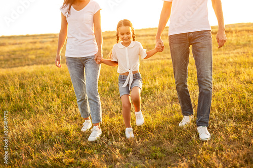 Cheerful daughter walking with anonymous parents in field