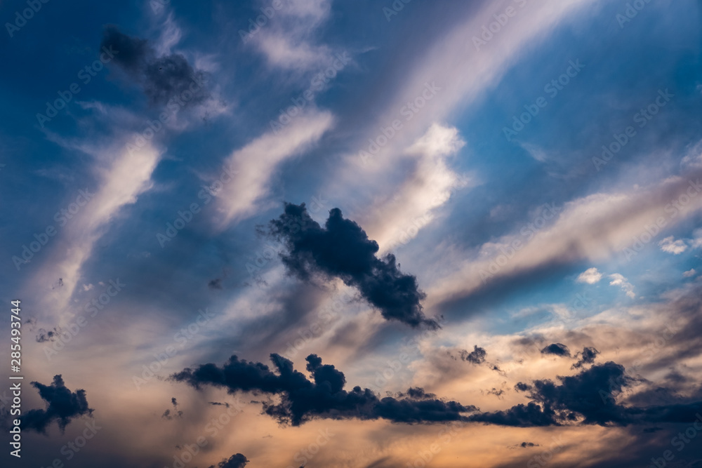 Evening sky at sunset background. Dark clouds hanging above horizon. Majestic cloudscape in blue, orange, violet shades. Grey cloudlets bringing rain. Countryside skyline in twilight time