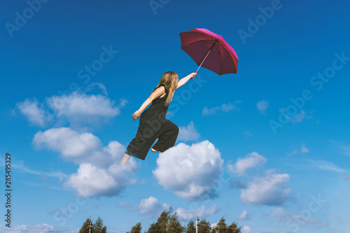 Cute girl jumping funny in clouds above earth. Small cheerful girl walking through sky with pink umbrella. Levitation concept