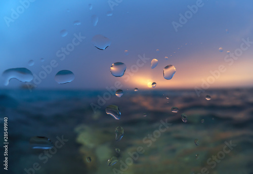 Fototapeta Naklejka Na Ścianę i Meble -  Drops of water on the glass against the background of the sea and the setting sun.