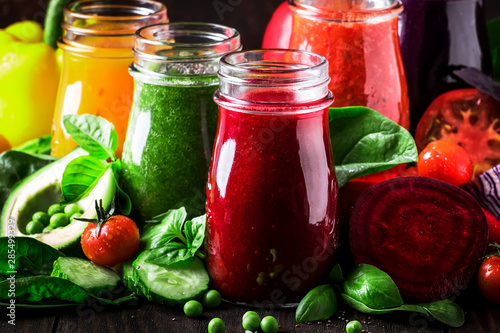 Multicolored vegan vegetable juices and smoothies from tomato, carrot, pepper, cabbage, spinach, beetroot in glass bottles on rustic kitchen table, vegetarian food and drink concept, selective focus