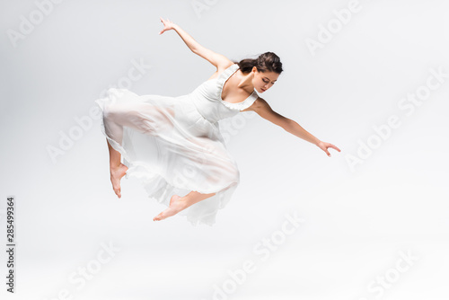 beautiful ballerina in white dress jumping in dance on grey background