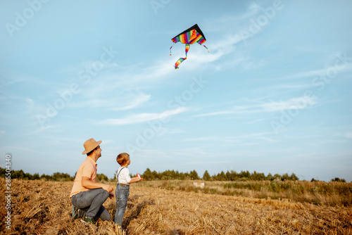 Father with son launching colorful air kite on the field. Concept of a happy family having fun during the summer activity