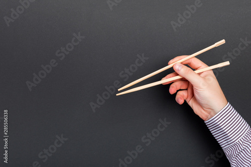 Fototapeta Naklejka Na Ścianę i Meble -  Male hand with chopsticks on black background. Traditional asian food with emty space for your design