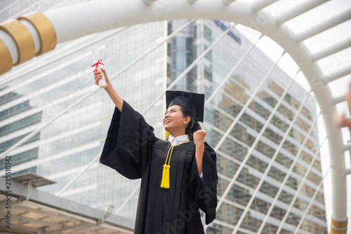 Happy Asian student woman winning graduate diploma and MBA degree in college,wearing academic dress and cap.Graduate Student and Success Education in University Concept.