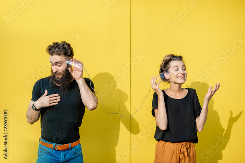 Man and woman talking with string phone made of cups on the yellow background. Concept of broken phone and bad communication