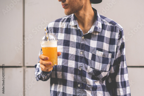 a guy holding a take away fruit smoothie glass with straw outdoors