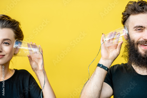 Man and woman talking with string phone made of cups on the yellow background. Concept of communication photo