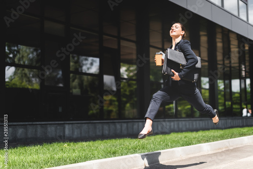 happy businesswoman levitating while holding briefcase and coffee to go