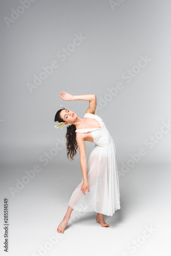 graceful, attractive ballerina in white dress dancing on grey background
