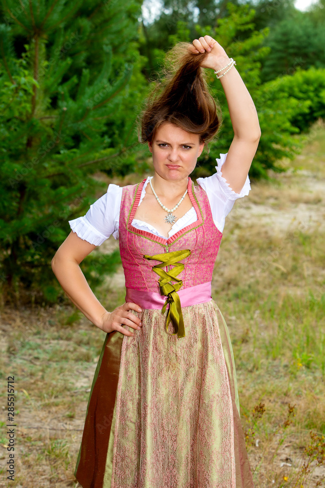 young woman in dirndl playing with her hair and making grimace young woman in dirndl playing with her hair and making grimace