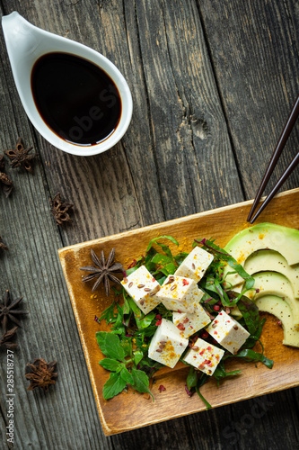 Tofu auf Teller und Holztisch mit Gemüse und bunten Früchten mit Sojasauce