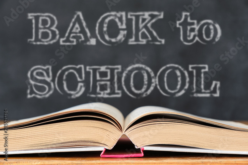 Back to School. Education concept with open book on wooden school desk against the school blackboard background