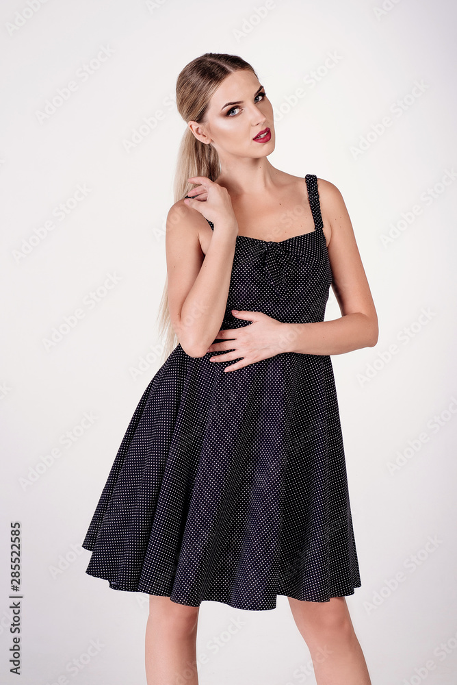 Young attractive sexy blond woman model with light hair, wearing short black dress and sandals on heels, posing and dancing in white studio Young attractive sexy blond woman model with light hair, wearing short black dress and sandals on heels, posing and dancing in white studio